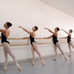 five ballet dancers practicing on a wall mounted ballet barre